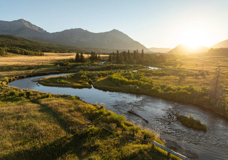 Majestic view of a serene river winding through lush greenery and mountainous terrain in Alberta, Canada, under dramatic clouds.