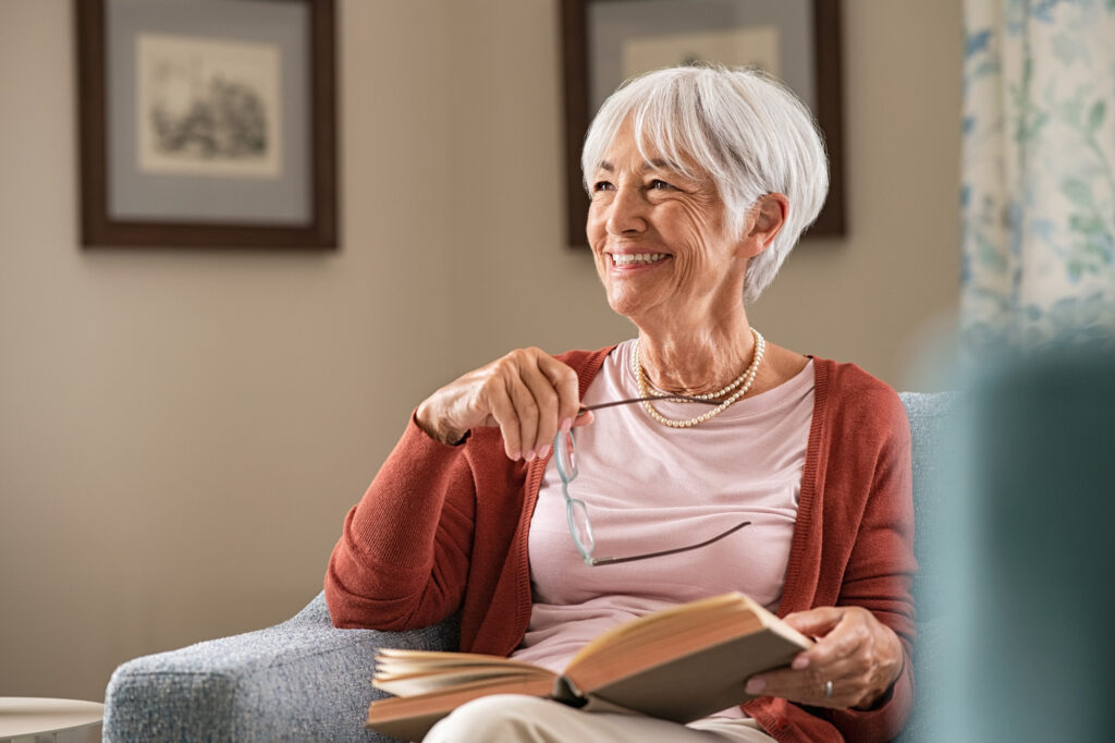 Woman smiling at home holding her glasses with a book