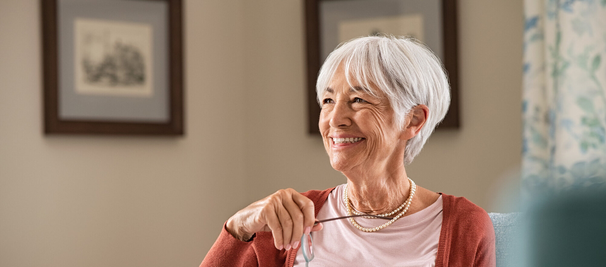 Woman smiling at home holding her glasses with a book