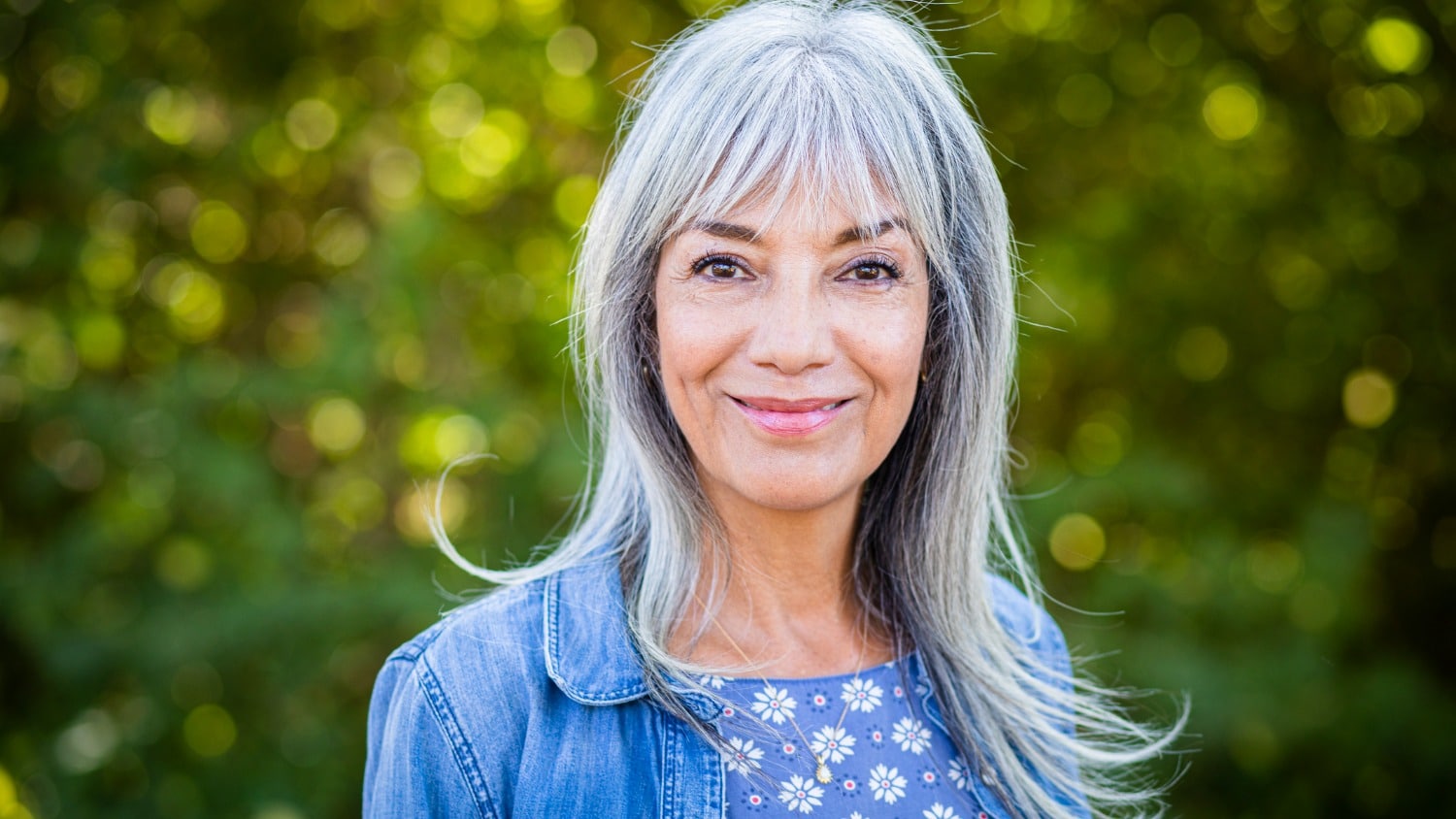 Woman with grey hair smiling at camera in beautiful natural setting