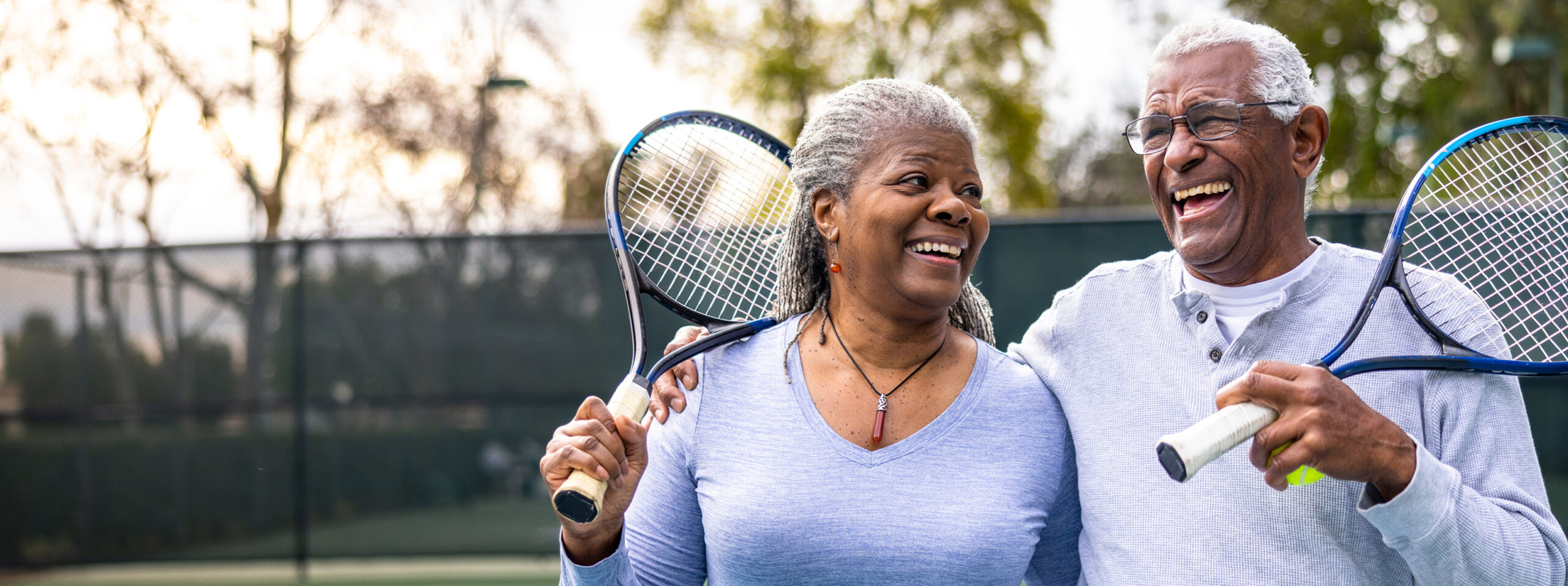 Two elderly people playing tennis outdoors smiling